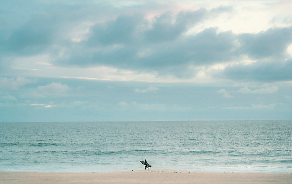 Photo of a single surfer walking along the shoreline in Manhattan Beach, CA.
