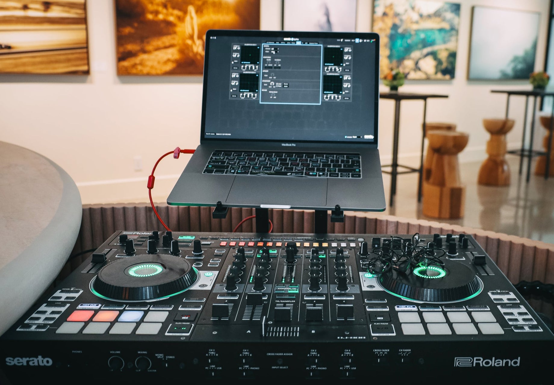 Roland DJ controller with laptop on a table in a room with artwork on the wall.