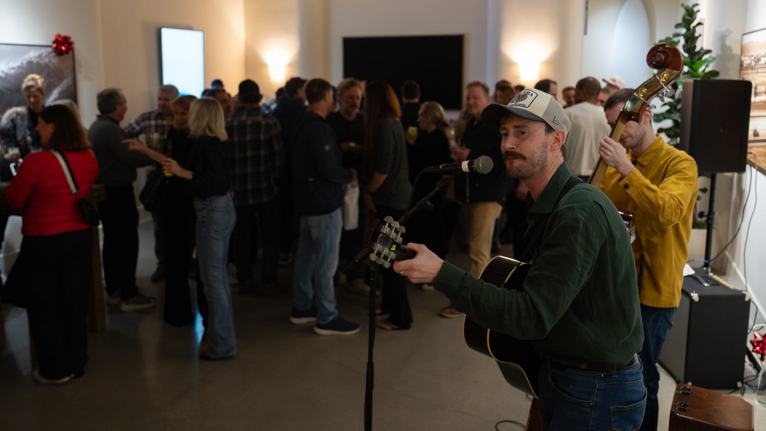 Man playing guitar in a room with people and art on the walls