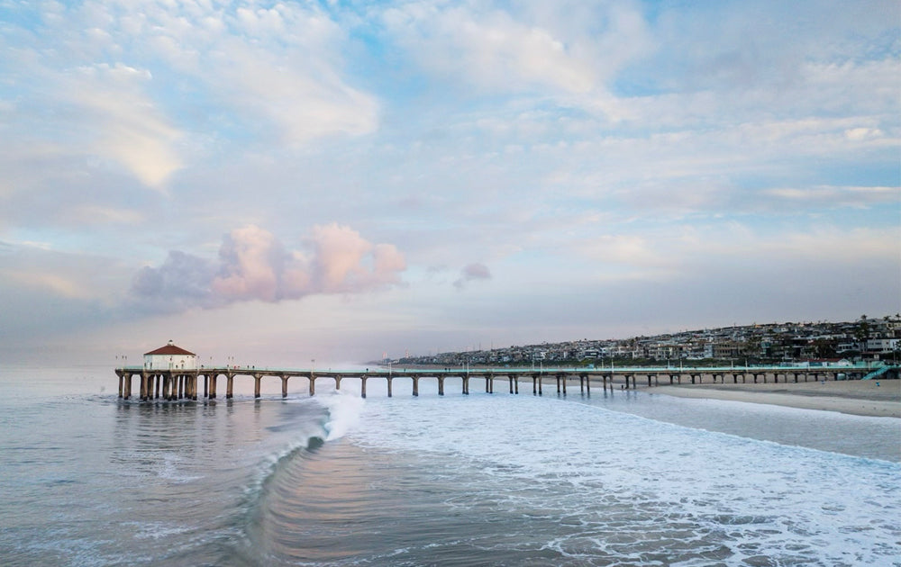Manhattan Beach Pier extending into the ocean with a cloudy sky above.