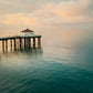 Manhattan Beach Pier with the red roof roundhouse building at the end extending into calm water under a cloudy sky.
