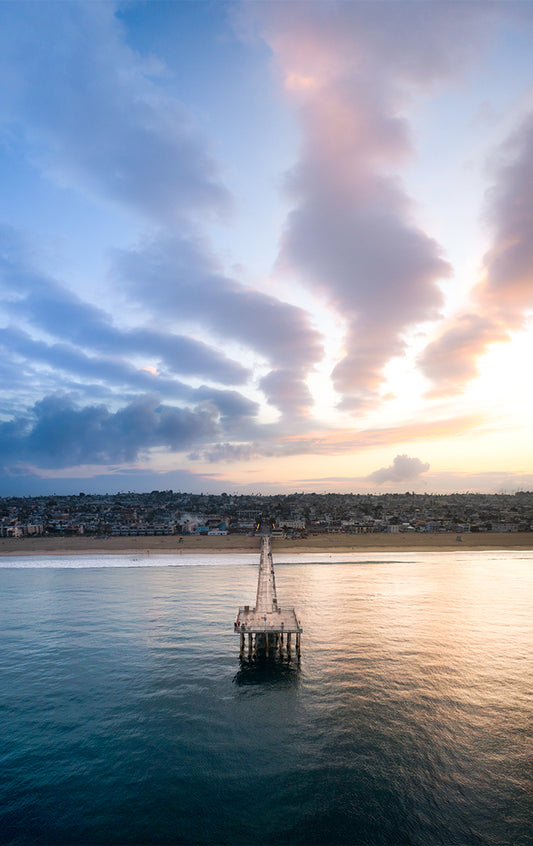 Hermosa Beach Pier extending into the ocean with a cityscape and colorful sky in the background.