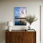 Wooden sideboard with a lamp, vase, and framed artwork on a wall.